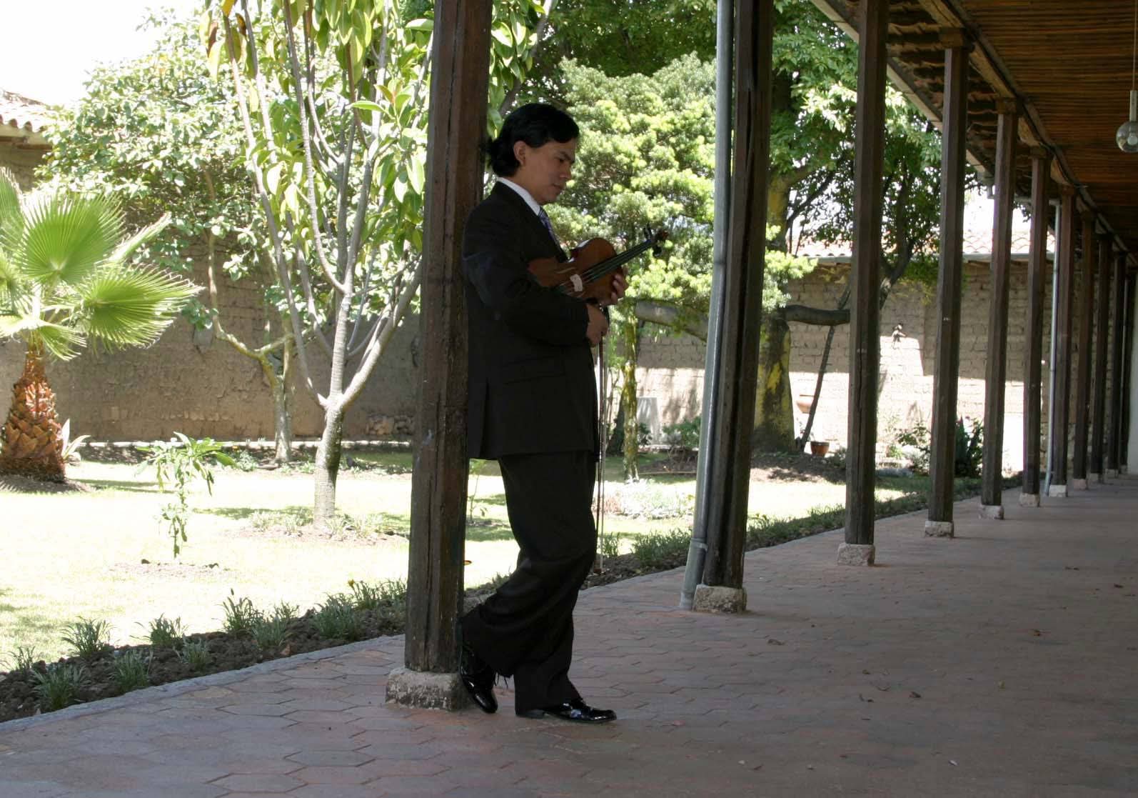 El maestro Patricio Mora afinando su violín en el jardín de una hacienda
